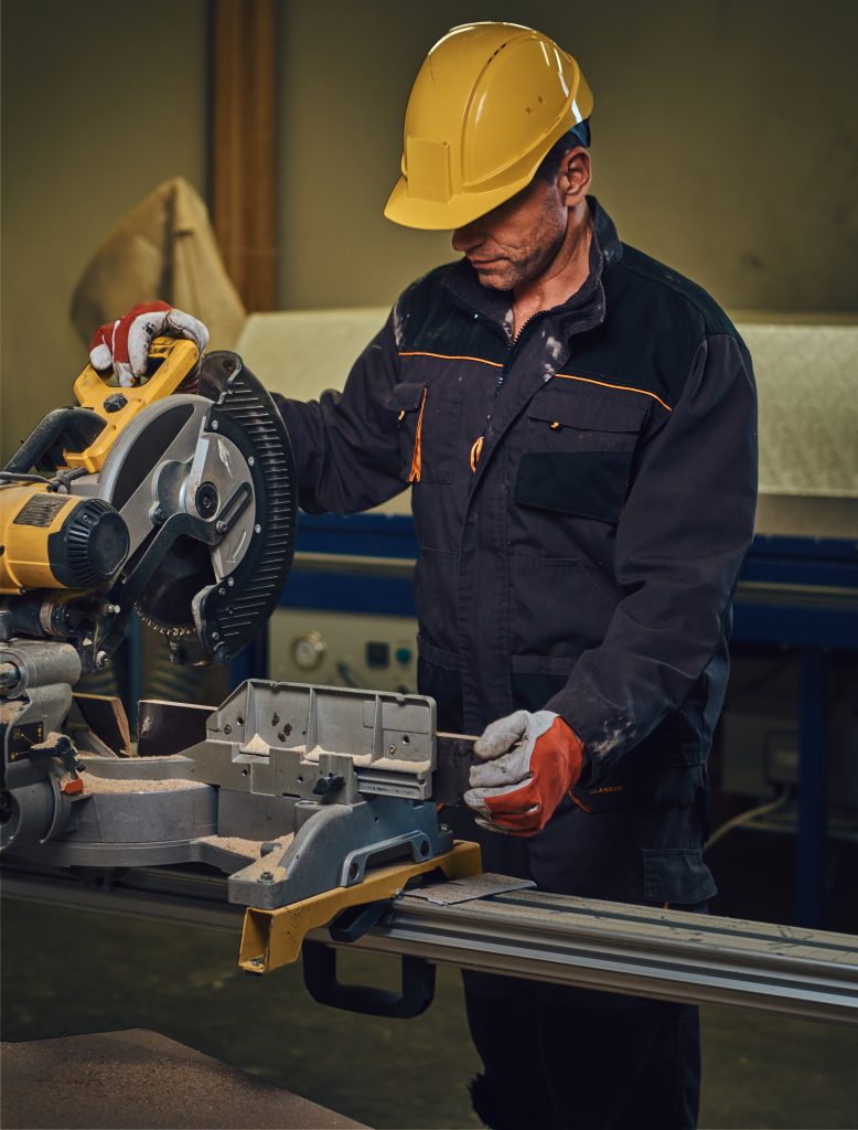carpenter male dressed safety yellow cap works with chain saw garage